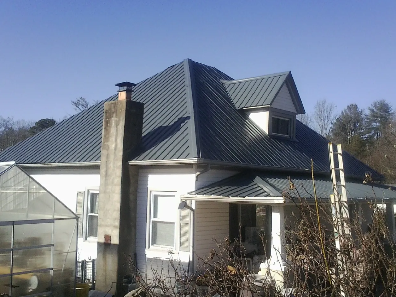 Dark blue standing seam metal roof on a white farmhouse with dormer — Slate & Tile Roof Repair by Roofing Brothers in Hazen