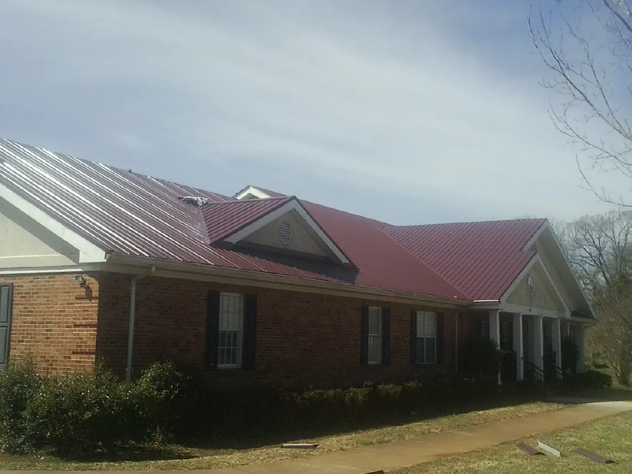Red metal roof with gabled entries on a long brick building, from a Hail Damage Roof Repair job in Hazen