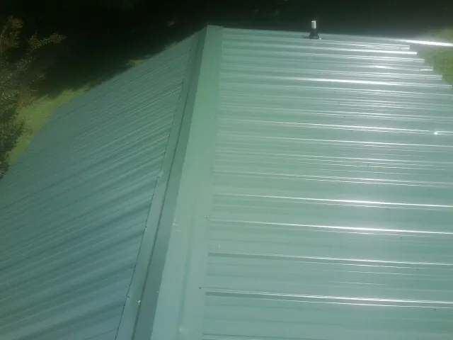New green metal panels meeting at the ridge of a roof — Flat Roof Repair work by our crew in Hazen