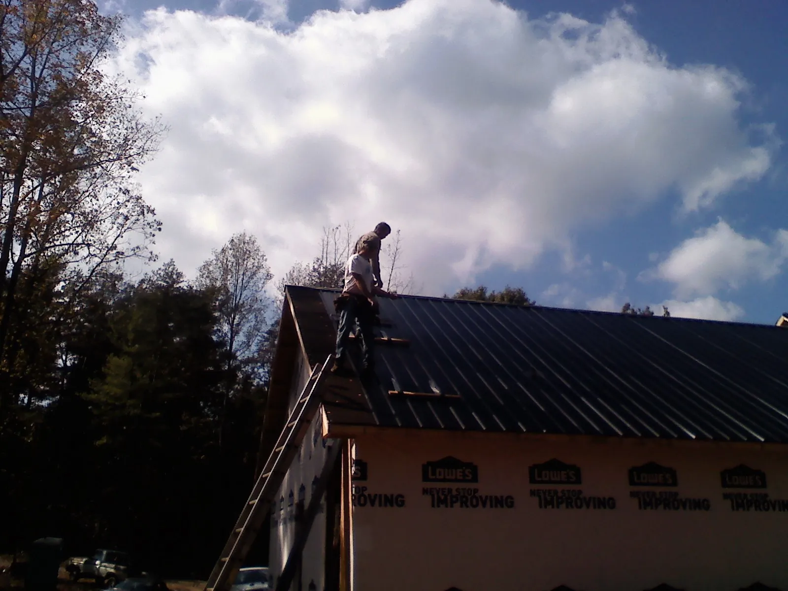 Roofer fastening dark metal panels high against a cloudy sky, from a Roof Inspection job in Hazen