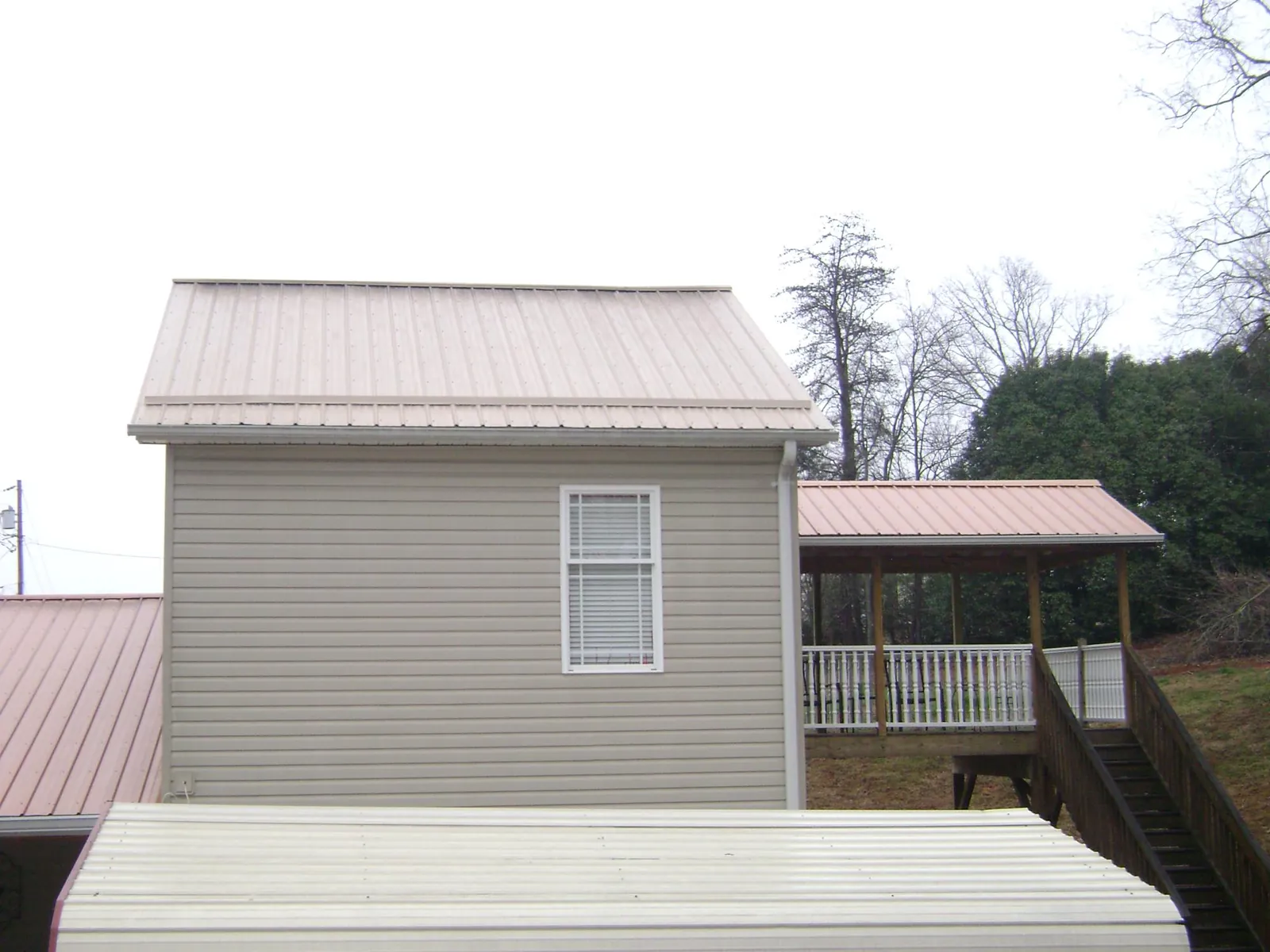 Tan metal roofs on a two story addition and attached porch, from a Roof Replacement job in Hazen