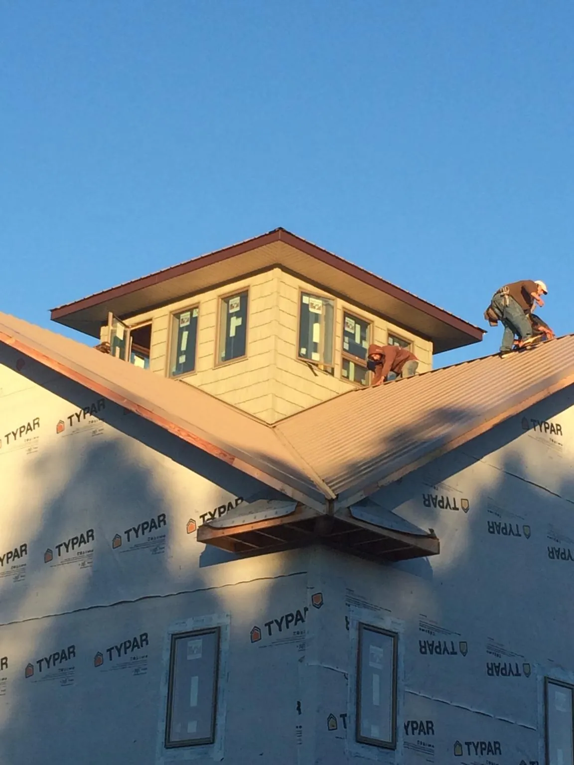 Roofers working around a rooftop cupola on a new metal roof at sunset in Hazen